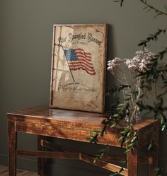 a wooden table topped with a vase filled with flowers next to a framed american flag