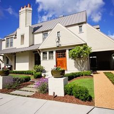 a white house with a red door surrounded by greenery and shrubs on a sunny day