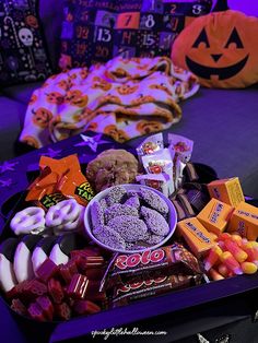 an assortment of halloween candy and candies in a black box on a purple couch