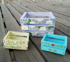 three painted wooden boxes sitting on top of a wooden table next to eachother