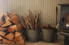 logs stacked next to each other in front of a wood burning stove and buckets with pine cones