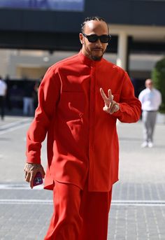 a man in an orange suit and sunglasses walks down the street with his peace sign