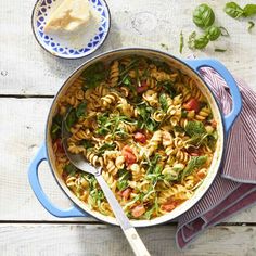 a pot filled with pasta and spinach on top of a wooden table next to bread