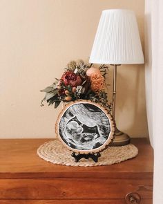 a lamp on top of a wooden dresser next to a vase with flowers and leaves