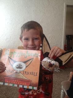 a young boy holding up a book with googly eyes