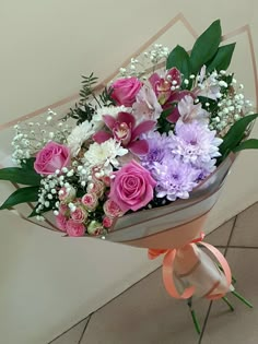 a bouquet of pink and white flowers is wrapped in paper on the floor next to a wall