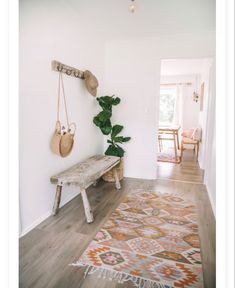 a wooden bench sitting in the middle of a room next to a rug and potted plant