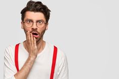 a man with glasses and suspenders making a surprised face while holding his hand to his mouth