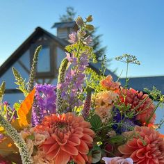 a vase filled with lots of colorful flowers on top of a wooden table in front of a house