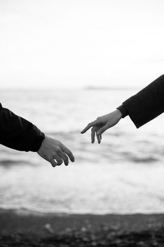 black and white photograph of two people reaching out towards each other, with the ocean in the background