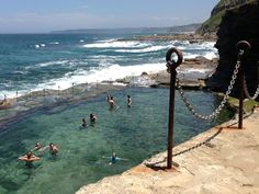 people are swimming in the ocean near some cliffs