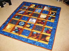 a blue and brown quilt on the floor with space related items all over it's surface