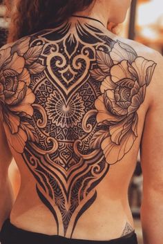 the back of a woman's body with tattoos on it and flowers in the center