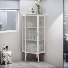 a white cabinet sitting in the corner of a room next to a vase with flowers