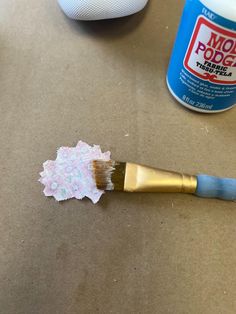 a paintbrush sitting on top of a piece of paper next to a can of glue