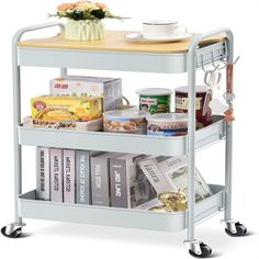 a metal cart filled with lots of books and other items next to a vase on top of a wooden table