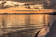 the sun is setting over the water and clouds are reflected in the calm waters at this beach