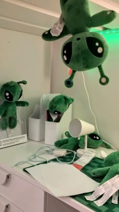 two green stuffed animals sitting on top of a white desk next to a lamp and other items