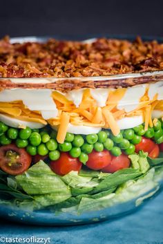 a layered salad in a glass dish with cheese and peas on the side, ready to be eaten