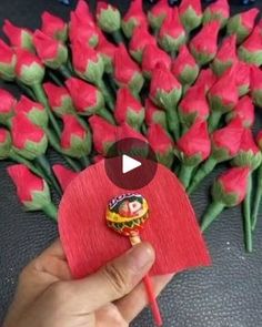 a hand holding a red piece of paper with flowers in the background and a video about how to make it