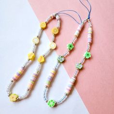 two necklaces with beads and flowers on them sitting on a pink and white surface