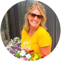 a woman in yellow shirt and sunglasses holding flowers