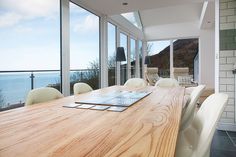 a large wooden table with white chairs in front of a window overlooking the ocean and mountains