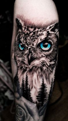 an owl with blue eyes and trees on his leg is seen in this tattoo design