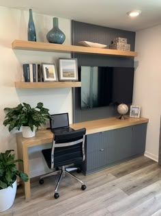 a desk with a laptop on it in front of a wall mounted entertainment unit and potted plants