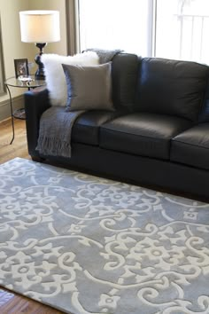 a living room with black leather couches and rugs on the floor in front of a window