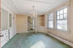 an empty room with a chandelier and two windows in the corner, next to a set of stairs