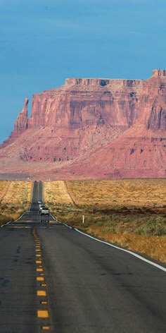 a truck driving down the road in front of a large rock formation with mountains behind it