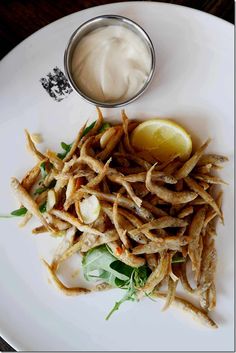 a white plate topped with fries and a lemon wedge next to a container of mayonnaise