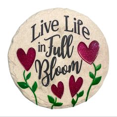 a stone with the words live life in full bloom written on it and red hearts surrounded by green leaves