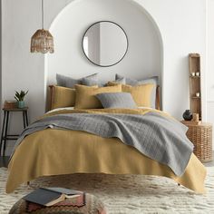 a bed with yellow and grey sheets in a bedroom next to a round mirror on the wall