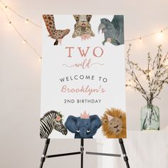 a welcome sign with animals on it in front of a white wall and string lights