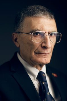 an older man wearing glasses and a suit in a dark room with his head turned to the side