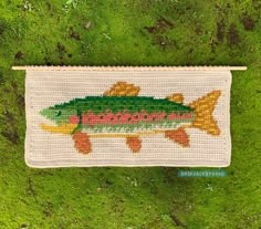 a crocheted rug with a fish on it in the middle of green grass