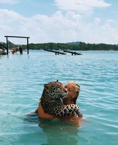 a woman in the water with a large leopard on her back, hugging her face