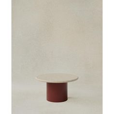 a round table with a red base on a white surface in front of a plain wall