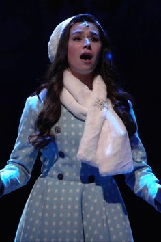 a woman in a blue dress and white hat with her hands out to the side