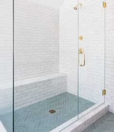 a walk in shower sitting next to a white tiled wall and floor with gold fixtures