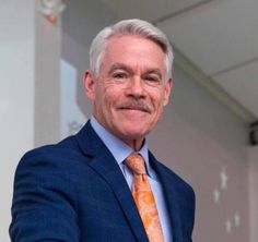 a man in a suit and orange tie posing for the camera with his arms crossed