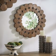 a mirror on the wall above a bowl of fruit and two candles in front of it