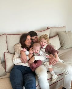 three adults and two children sitting on a couch with one holding a baby in the other's lap