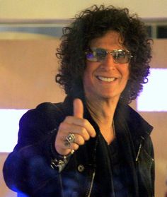 a man with curly hair giving the thumbs up sign while wearing sunglasses and a leather jacket