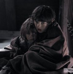 two people wrapped up in blankets sitting on the floor with one person looking at the camera