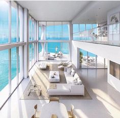 a living room filled with lots of white furniture next to large windows overlooking the ocean