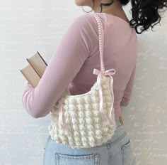 a woman holding a book in her right hand while wearing a crocheted purse