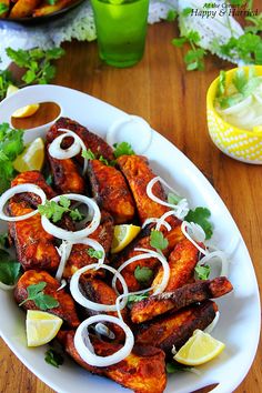 a white plate topped with chicken wings covered in onions and cilantro next to lemon wedges